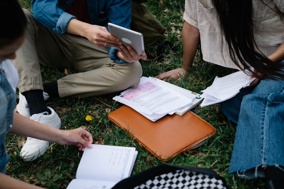 A group of students studying together outside, using a tablet and papers on the grass.